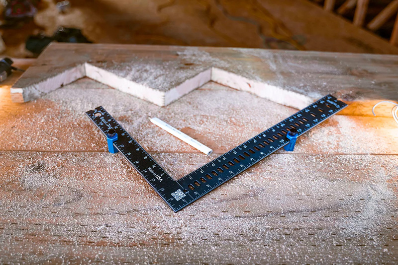 Freshly cut stair stringer with a blue framing square and stair gauges placed on it.