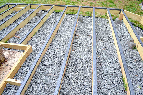 Ground-level deck frame made of pressure-treated lumber, sitting on concrete blocks with a gravel base underneath.