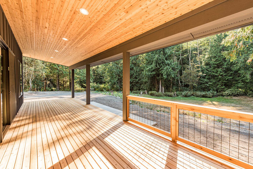 Ground-level wooden deck with a full roof, tongue-and-groove soffit, wooden handrails, and metal wire accents.