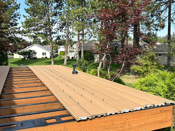 Pressure-treated deck frame with composite deck boards halfway installed, close to the ground.