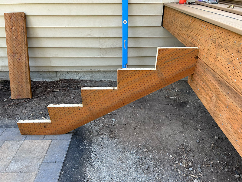 Pressure-treated stair stringer attached to a deck and landing on a paver patio.