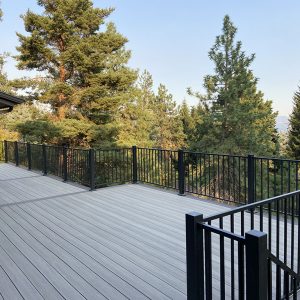 Spacious custom deck across the back of a home, surrounded by a scenic backdrop of tall pine trees.